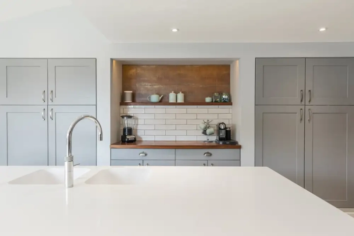 Modern shaker kitchen with grey built-in cabinets, white quartz island with chrome tap, subway tile backsplash, wooden countertop, and open shelf with pastel kitchen accessories