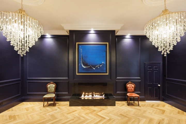Art gallery with indigo walls with paneling, bioethanol fire below an oil painting and chandeliers