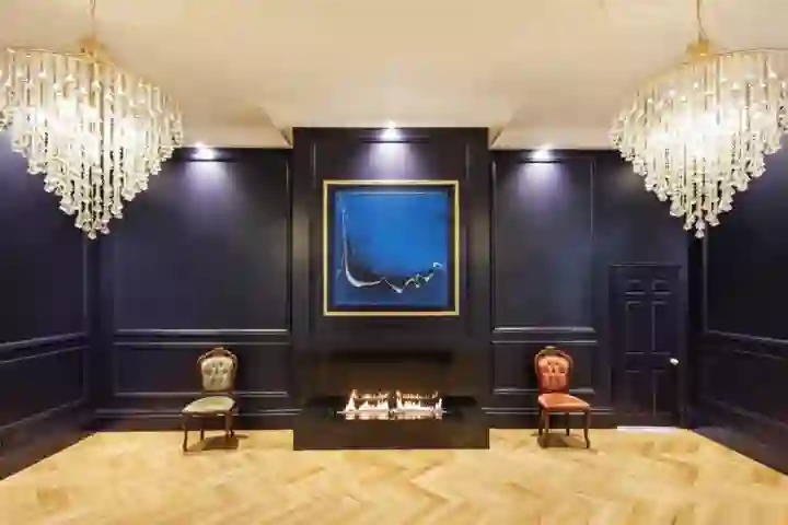 Art gallery with indigo walls with paneling, bioethanol fire below an oil painting and chandeliers