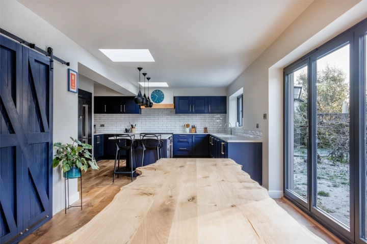 Raw edge wooden dining table in modern kitchen with blue shaker style cupboard doors with skylights