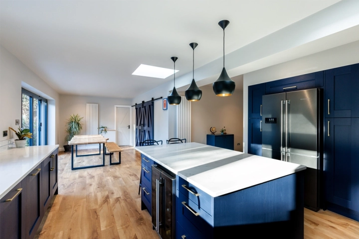Modern kitchen diner with large central island with white quartz worktop. Black pendant lights