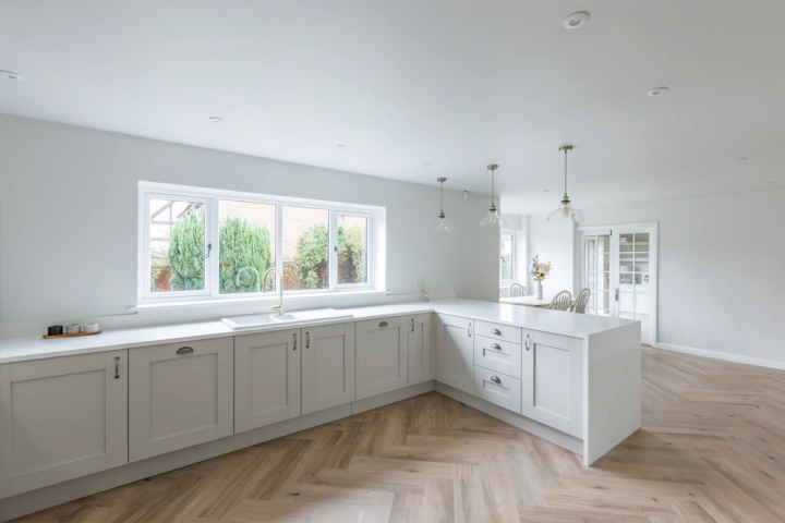 Open-plan kitchen leading to a dining area with wooden table and upholstered chairs, illuminated by natural light through bi-fold doors.