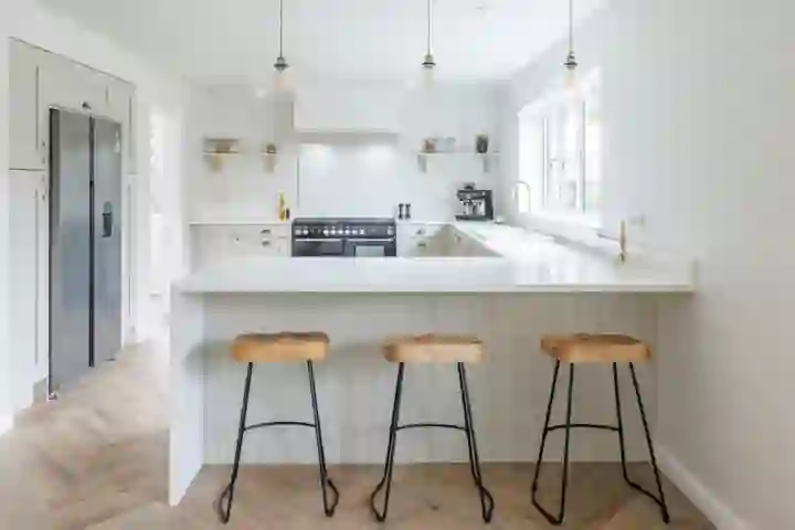 Open-plan kitchen leading to a dining area with wooden table and upholstered chairs, illuminated by natural light through bi-fold doors.