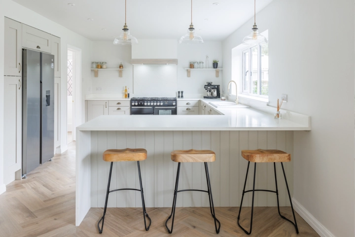 Open-plan kitchen leading to a dining area with wooden table and upholstered chairs, illuminated by natural light through bi-fold doors.