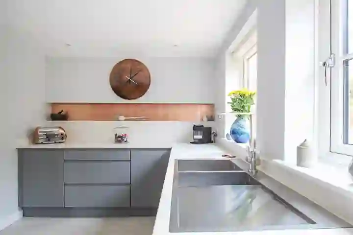 Modern kitchen with white worktop and grey cabinets and striking copper tile splashbacks in built in recesses