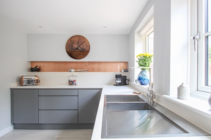 Modern kitchen with white worktop and grey cabinets and striking copper tile splashbacks in built in recesses