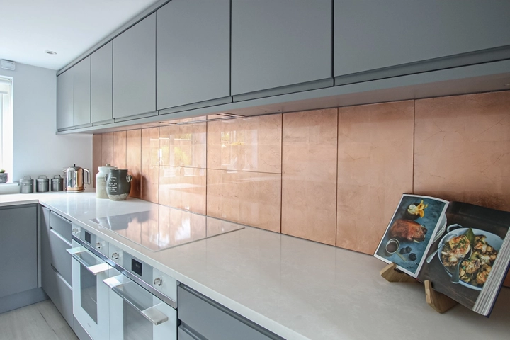 Modern kitchen with white worktop and grey cabinets and striking copper tile splashbacks in built in recesses