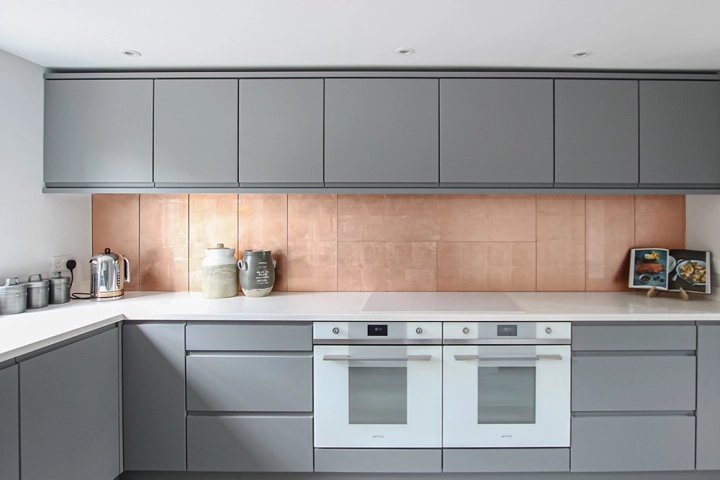 Modern kitchen with white worktop and grey cabinets and striking copper tile splashbacks in built in recesses