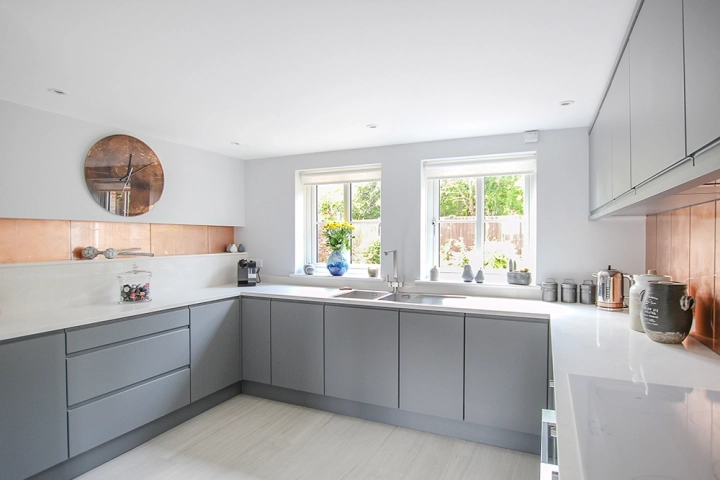Modern kitchen with white worktop and grey cabinets and striking copper tile splashbacks in built in recesses