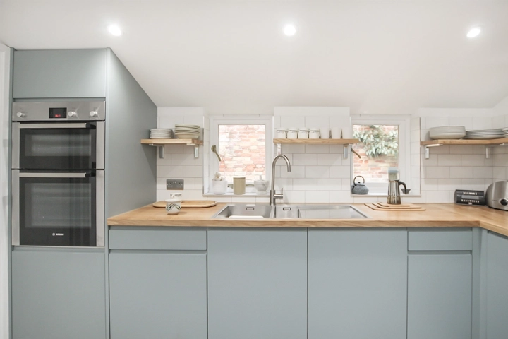 Contemporary kitchen with sky light, oak worktops and modern light blue doors, stainless steel sink and oven canopy