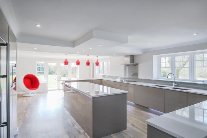 Large modern kitchen with white countertops, chrome detail and red pendant lights